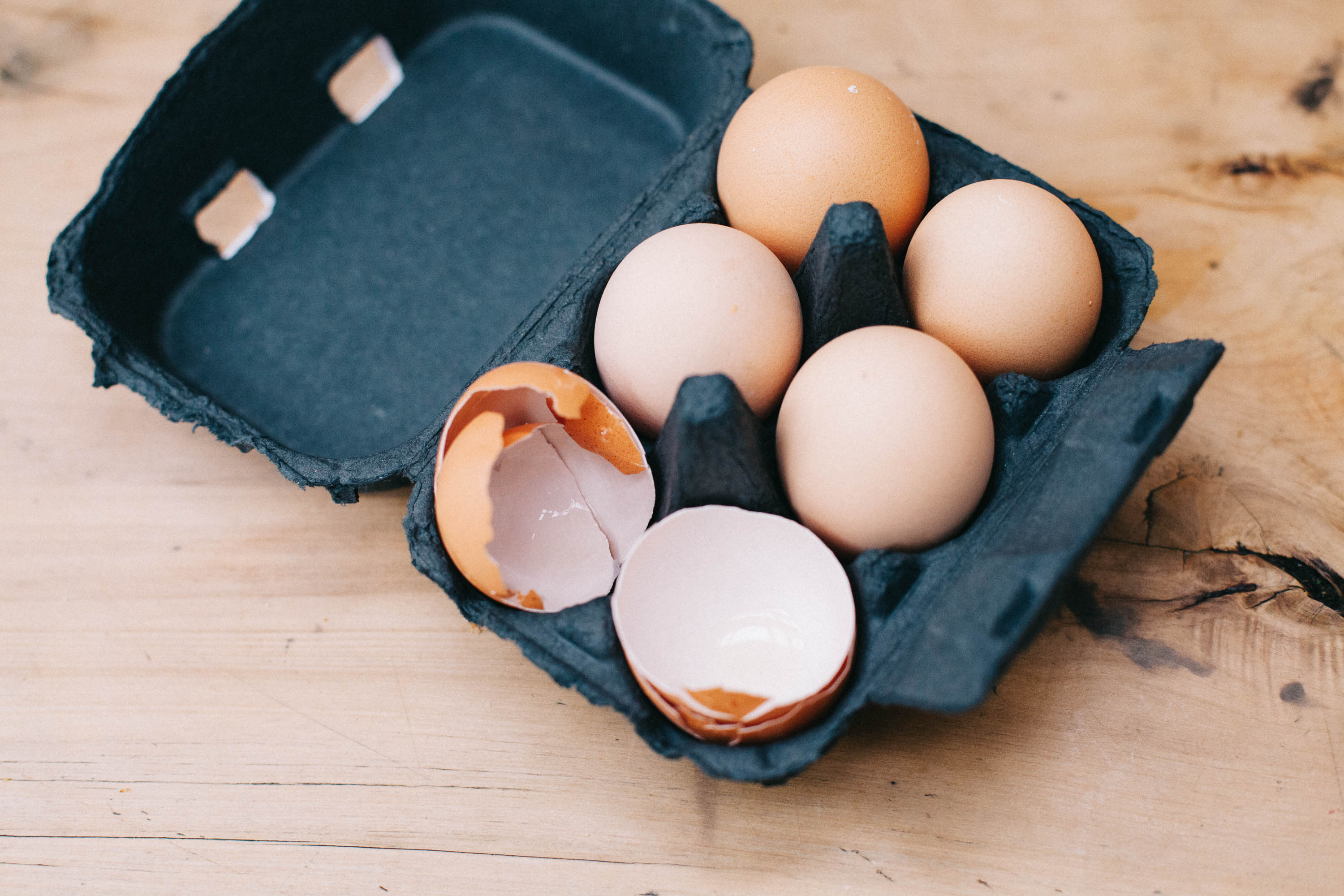 4 eggs and 2 empty egg shells in a black egg container on a wooden bench (c) Leonie Wise