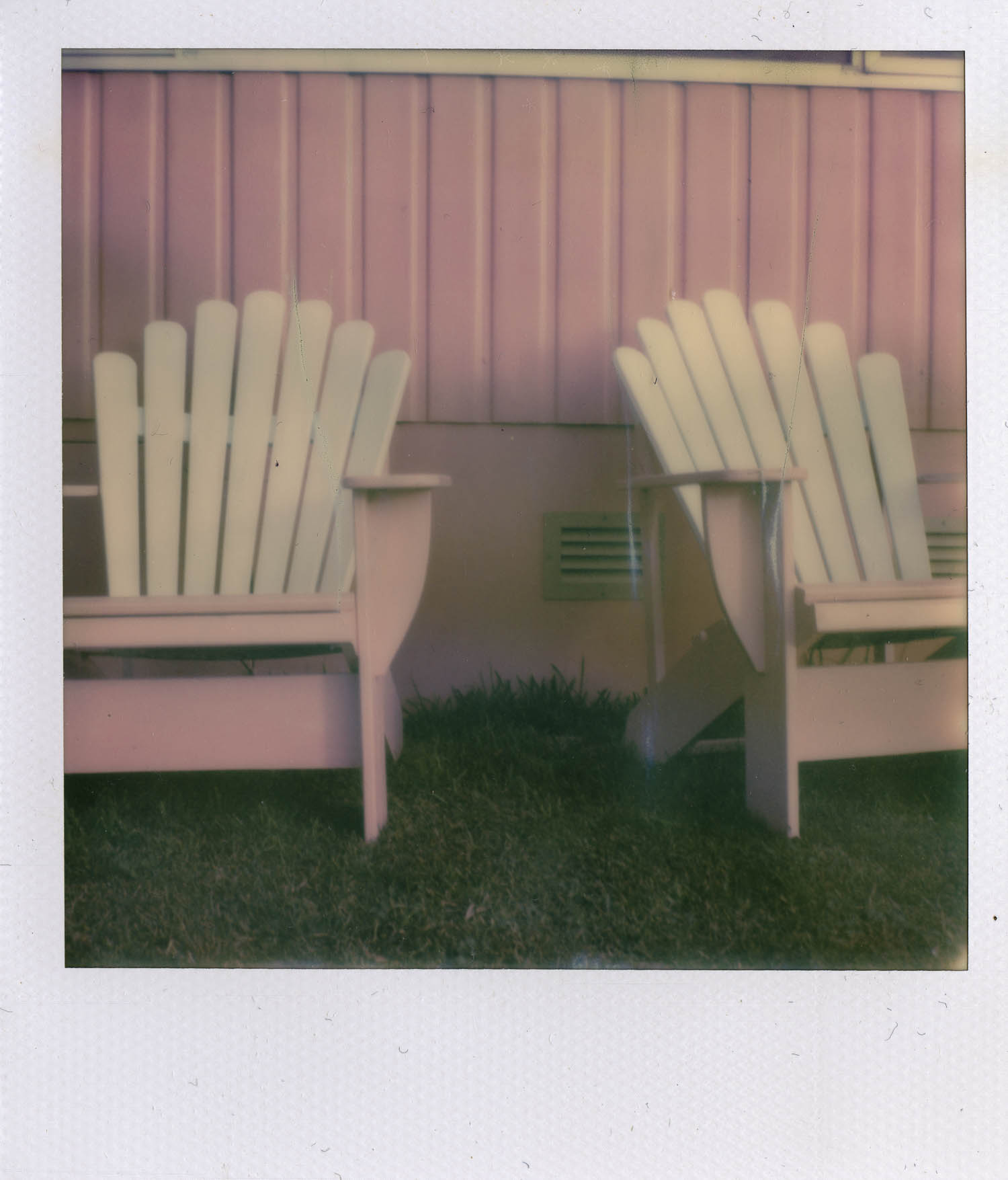 photograph of pink weatherboard on the side of a house with two pink and white adirondack-style chairs on the grass in front of the building. © leonie wise