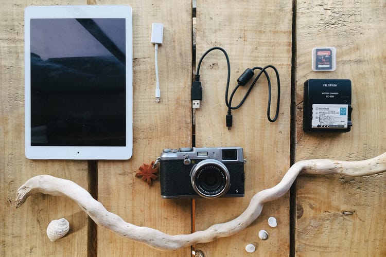 Fuji x100s camera, Ipad, Battery Charger, Memory cards and USB cable on a table. By leonie wise