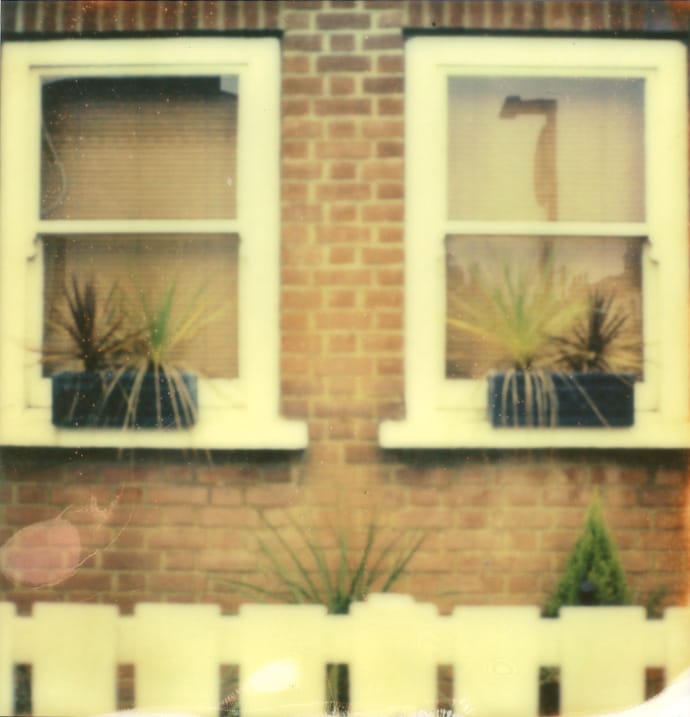 polaroid photograph of two windows and the top of a picket fence. copyright leonie wise