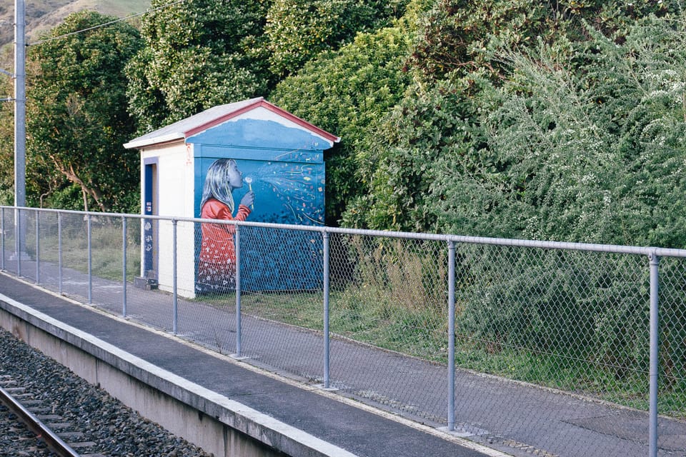 a moment unravelling time: a mural of a girl blowing a dandelion clock on the wall of a building beside a railway line. (c) l