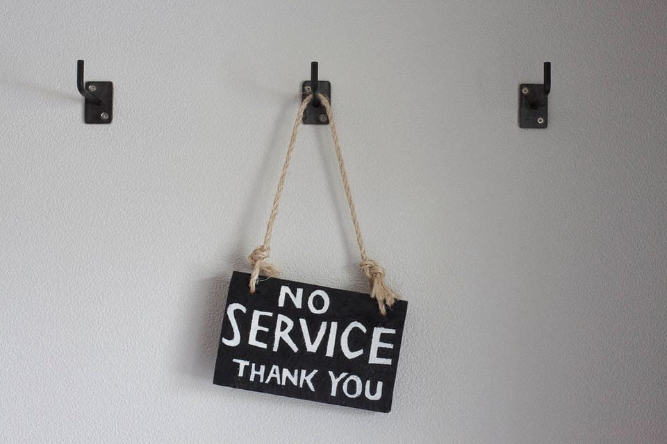 Chalk board sign that says "No service thank you" hanging from a hook by a string