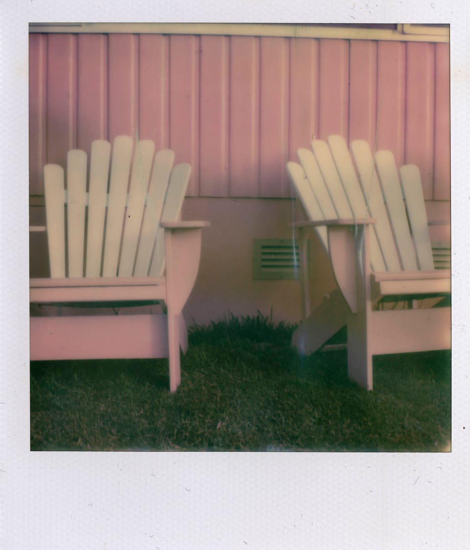 photograph of pink weatherboard on the side of a house with two pink and white adirondack-style chairs on the grass in front 